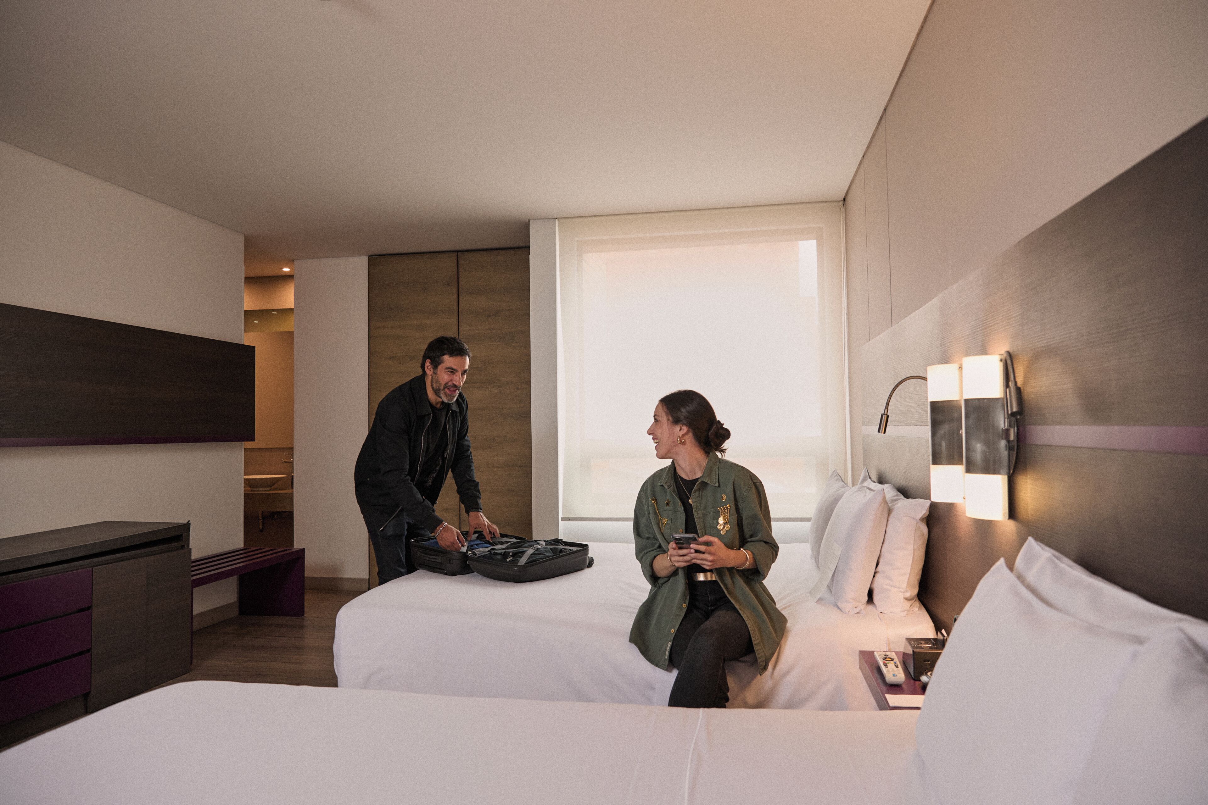Et hotelværelse med en seng, et natbord, et skrivebord og et vindue.