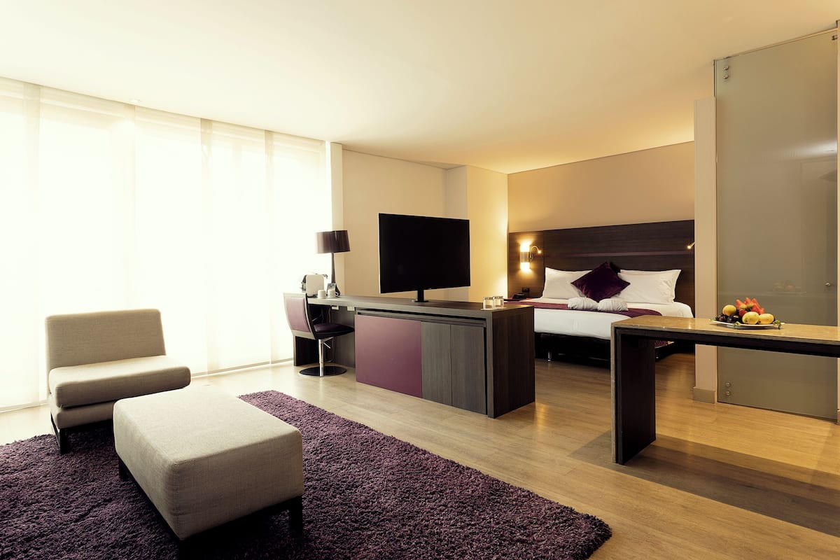 Habitación de hotel con cama, escritorio, silla, televisor y un amplio ventanal.