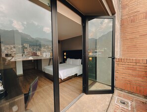Une chambre d’hôtel avec un lit, un bureau et une vue sur le paysage urbain, visible à travers une porte vitrée.