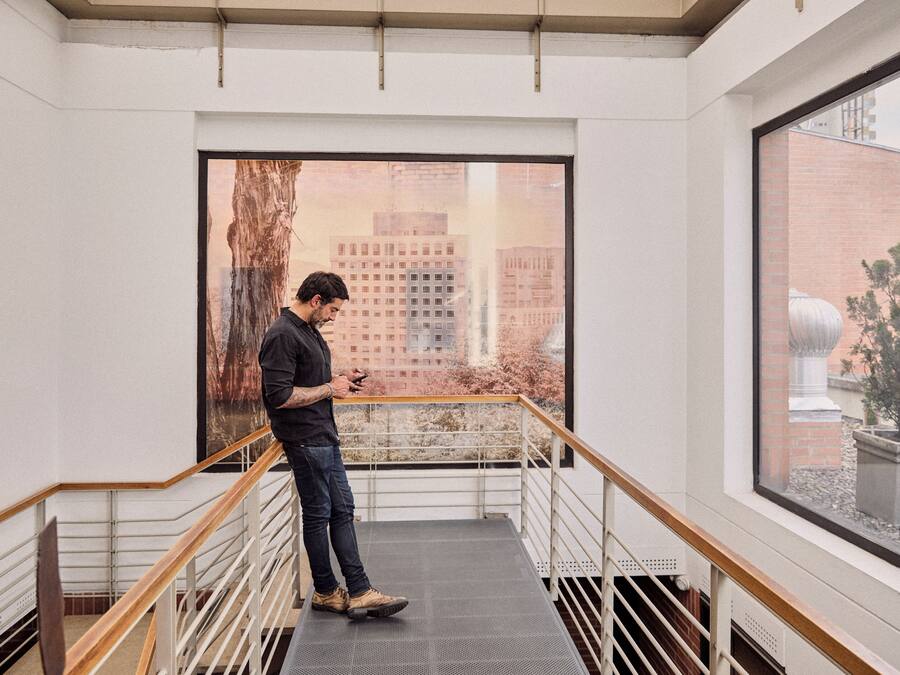 A man standing on a staircase with a city view through a large window.