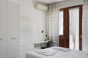 Une chambre d’hôtel comprenant un lit, un bureau avec une chaise, un appareil de climatisation et une fenêtre avec des rideaux.
