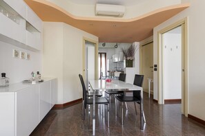 Une cuisine moderne avec des meubles blancs, une table à manger avec des chaises et un couloir menant à une porte.