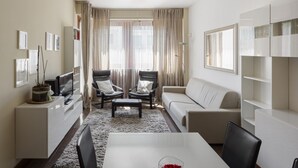 A modern living room with a sofa, two armchairs, a coffee table, a TV, and a bookshelf. - Hostmate - Milano - Teodorico (Milano)