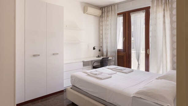A bedroom with a bed, a desk, a chair, a wardrobe, and a window with curtains. - Hostmate - Milano - Teodorico (Milano)