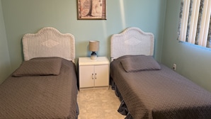 A bedroom with two single beds, a nightstand with a lamp, a framed picture on the wall, and a window with blinds. - Sunny Apartments a block from Warm Mineral Springs. Unit 3 (North Port)