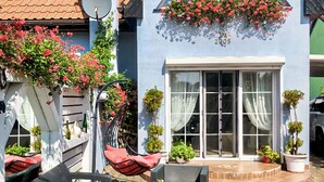 Ein blaues Gebäude mit einem großen Fenster, einer Tür, Blumentöpfen und Außenplätzen.