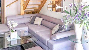 Ein modernes Wohnzimmer mit einem grauen Ecksofa, einem Glastisch und einer weißen Vase mit violetten Blumen.