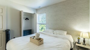 Una camera da letto con un letto, un comodino con una lampada, una finestra con persiane, un termosifone e un armadio.