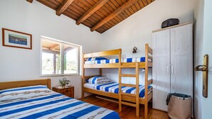 Ein Zimmer mit einem Etagenbett, einem Einzelbett, einem Kleiderschrank, einem Fenster und einem kleinen Tisch mit einer Pflanze.