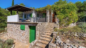 Ein Steinhaus mit grüner Tür, einem Balkon mit Gartenmöbeln und einer Treppe, die zu einer höheren Ebene führt.