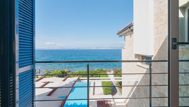 Un balcon avec vue sur la mer, une piscine et un bâtiment en pierre.
