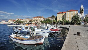 Un port de plaisance où sont amarrés plusieurs bateaux, une promenade en bord de mer et des bâtiments historiques coiffés de toits en tuiles rouges.