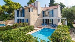 Une maison à deux étages dotée d’une piscine, d’un patio couvert et d’une façade en pierre.