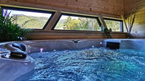 Un jacuzzi con una escultura de piedra, techo de madera y ventanas con vistas a un bosque.