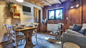 Una sala de estar acogedora con techo de madera, una zona de comedor con mesa y sillas de madera, un sofá gris y una ventana con vistas a zonas verdes.