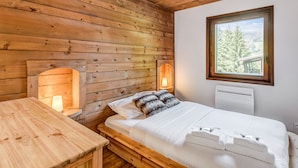 Quarto de cabana de madeira com cama, mesa de cabeceira, janela e aquecedor fixado na parede.