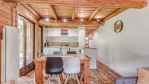 Interior acolhedor de uma cabana com mesa de jantar de madeira, duas cadeiras, um sofá e uma cozinha com micro-ondas e pia.