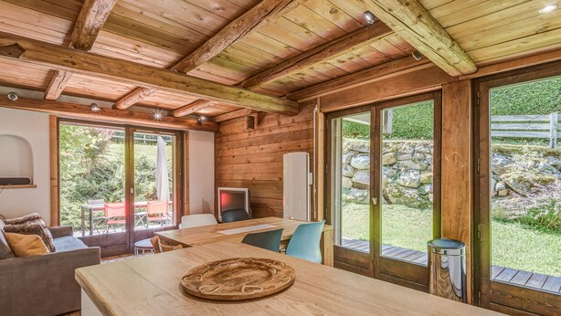 Interior de uma cabana de madeira com área de jantar, um sofá e vista para o jardim através de grandes portas deslizantes.