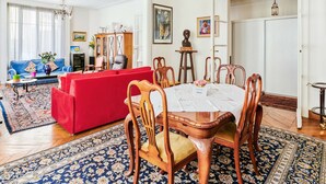 A spacious living room with a red sofa, wooden dining table, and a chandelier. - Appartement Carpette - Welkeys (Paris)