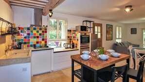 Une cuisine compacte avec des meubles blancs, un crédence aux couleurs vives et un coin repas comprenant une table et des chaises en bois.
