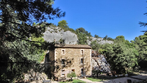 Un bâtiment en pierre doté de nombreuses fenêtres et d’un petit jardin agrémenté d’un banc.