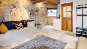 Une chambre rustique avec un mur en pierre, un lit agrémenté d’oreillers à motifs, une petite table en bois et une vue sur l’extérieur par une fenêtre.