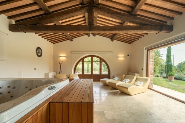 A spa room with a hot tub, wooden bench, and a seating area with a view of the garden.