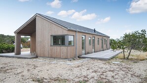 A modern wooden cabin with a sloped roof and large windows, situated on a sandy terrain with sparse vegetation. - Amazing home in Anholt with WiFi (Anholt)