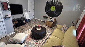 A modern living room with a sofa, a coffee table, a TV, and a unique cityscape wall art. - Breaking Records - Steps from Paristown Hall (Louisville)
