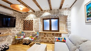 A cozy living room with stone walls, wooden beams, a TV, a wine rack, and colorful chairs. - Cozy home in Kaprije with kitchen (Kaprije)