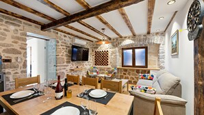 A dining area with a stone wall, wooden beams, a TV, and a dartboard. - Cozy home in Kaprije with kitchen (Kaprije)