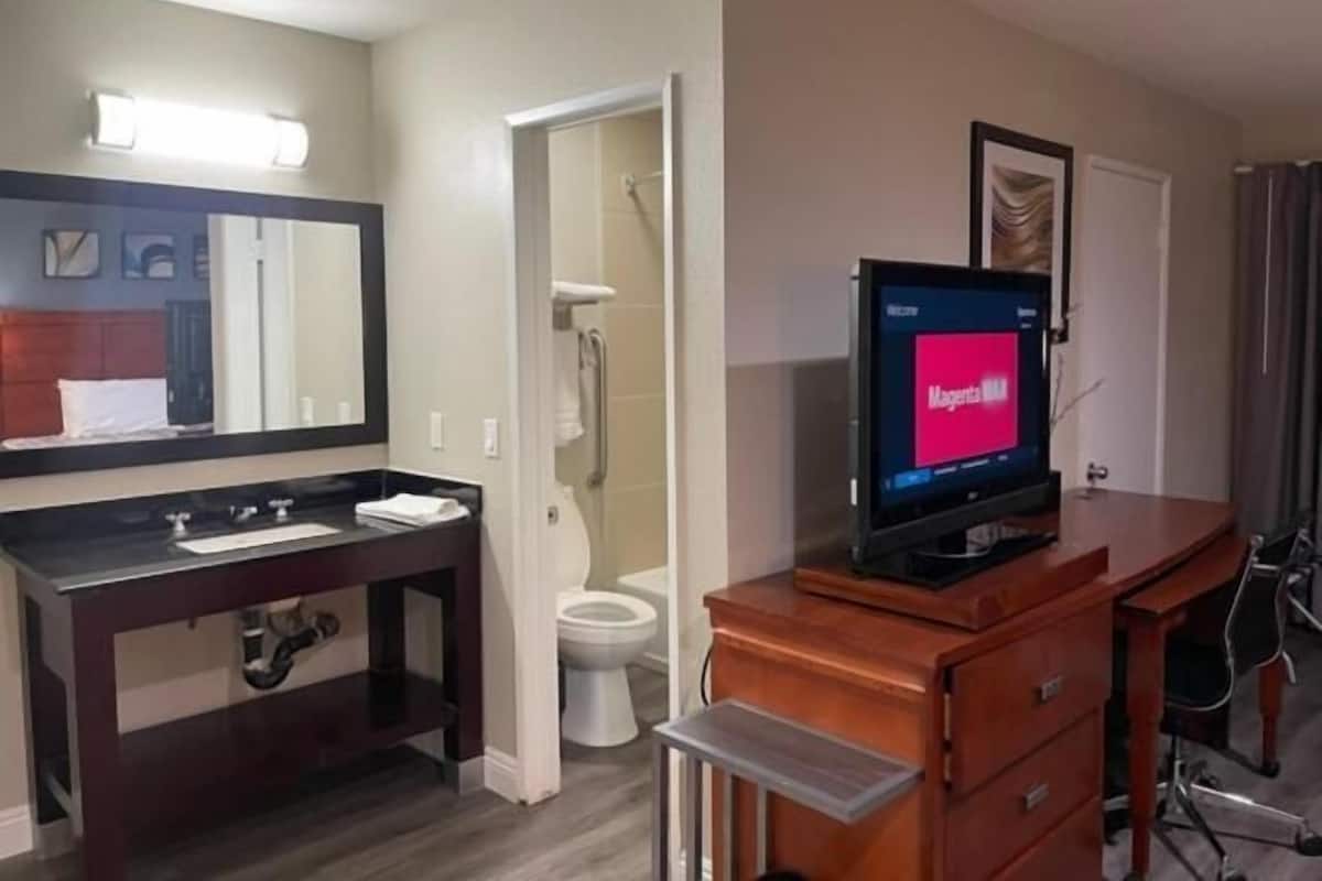 Ein Hotelbad mit Waschbecken, Spiegel, Toilette, Dusche und einem Fernseher, der 'Magenta TV' anzeigt.