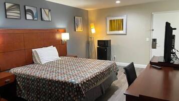 A hotel room with a bed, a desk, a TV, and a lamp.