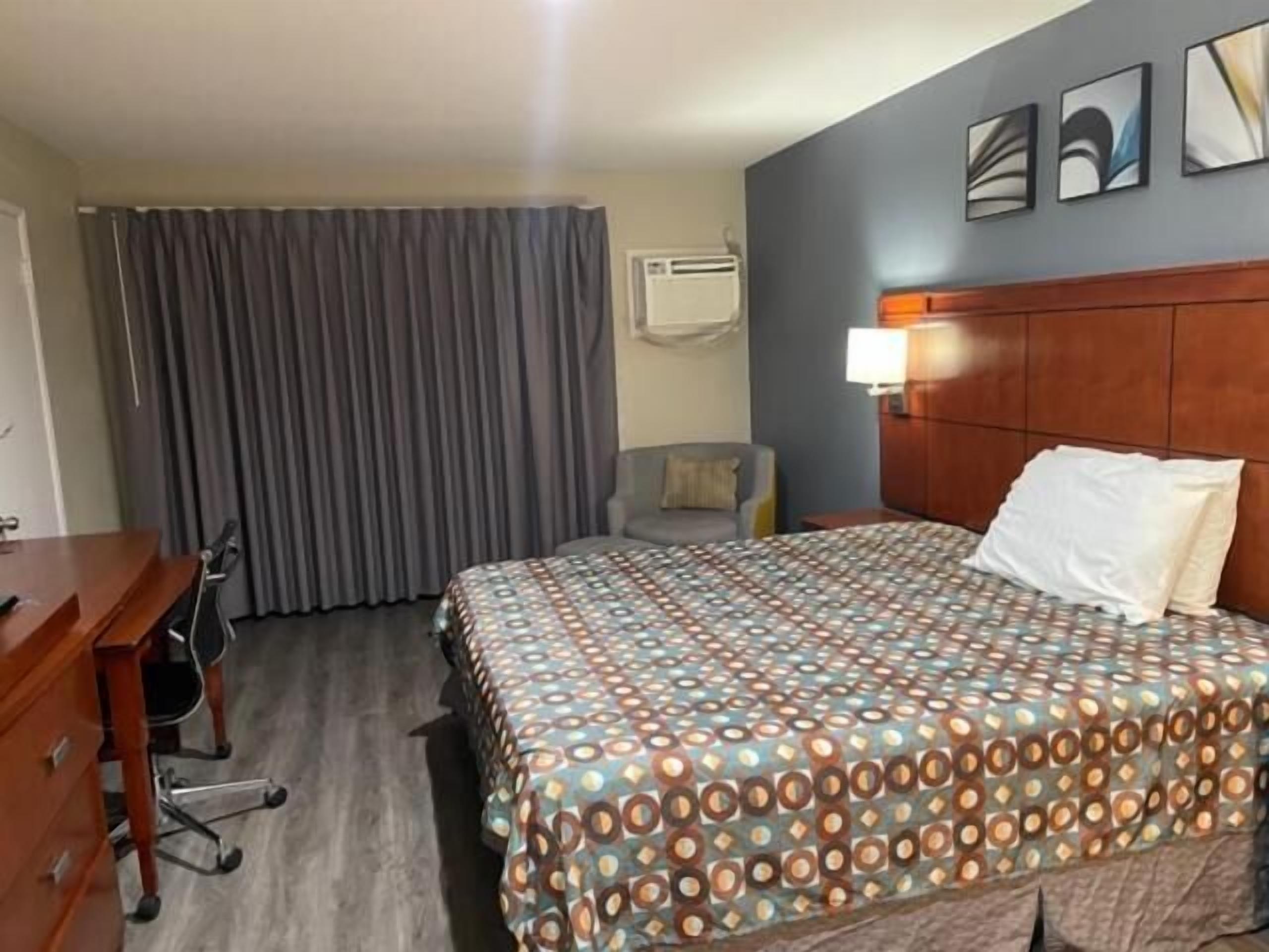 A hotel room with a bed, a desk, a chair, and a window with curtains.