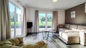 Ein geräumiges Wohnzimmer mit großem Fenster, einer Couch, einem Couchtisch und einem Fernseher.
