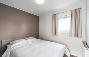 Simple, functional room with a single bed and a window with beige curtains.