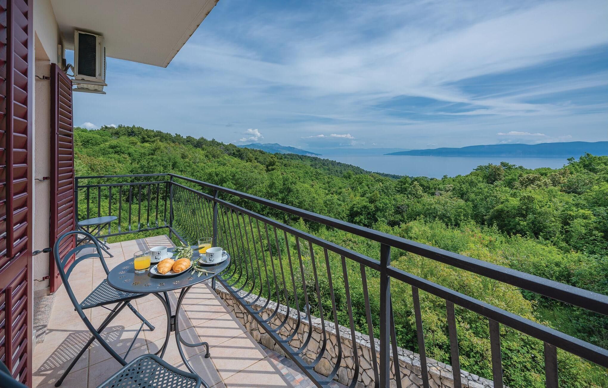 Ein Balkon mit Frühstückstisch, mit Blick auf eine üppige grüne Landschaft und ein Gewässer.