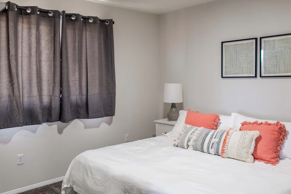 A bedroom with a bed, curtains, a nightstand, a lamp, and two framed pictures on the wall.