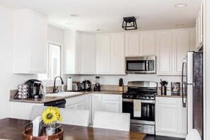 A modern kitchen with white cabinetry, a granite countertop, a built-in microwave, a stove, and a refrigerator.