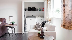 A compact living space with a sofa, a small round table, a coffee table, and a laundry area with washing machines and dryers.