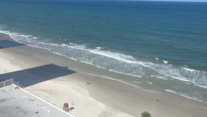 Een strand met een heldere lucht, rustige zee en een verharde promenade.