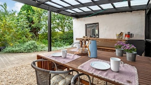 Eine Terrasse im Freien mit Holztisch, gedeckt für das Essen, umgeben von viel Grün und einer Pergola mit Metallverkleidung.