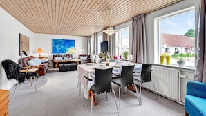 Ein modernes Wohnzimmer mit Essbereich, mit Holzboden, großen Fenstern und Blick ins Freie.