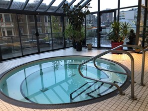 An indoor swimming pool with a glass ceiling, surrounded by potted plants and a tiled floor.