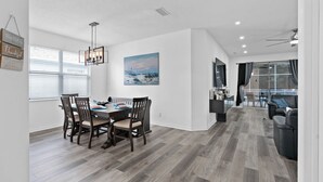 A modern dining area with a wooden table and chairs, a chandelier, and a painting on the wall. - 4 Bedrooms/2 Bathrooms AMAZING HOME! PRIVATE POOL! (Kissimmee)