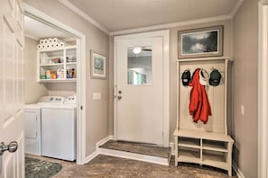 Une buanderie équipée d’un lave-linge et d’un sèche-linge, une porte donnant sur un couloir et un porte-manteau avec des vestes.