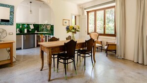Un coin repas avec une table et des chaises en bois, un vase rempli de fleurs et une vue sur l’extérieur par une fenêtre.