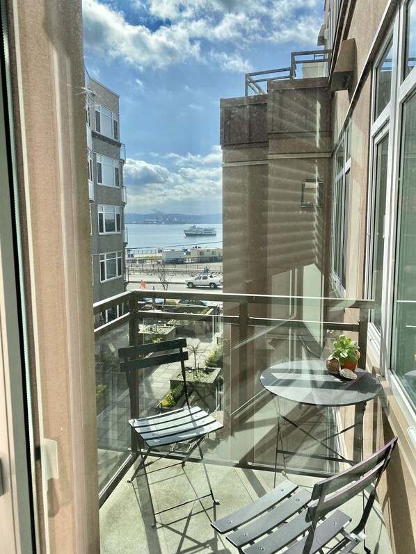 A balcony with a glass table, chairs, and potted plants.