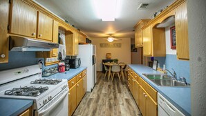 A compact kitchen with wooden cabinets, a gas stove, a refrigerator, and a dining area with a table and chairs. - Simplicity (Broken Bow)