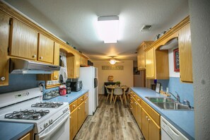A compact kitchen with wooden cabinets, a gas stove, a refrigerator, and a dining area with a table and chairs. - Simplicity (Broken Bow)